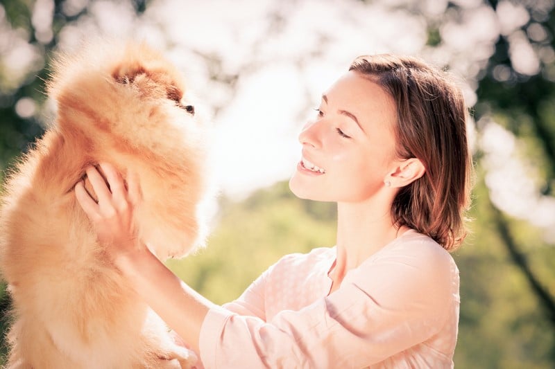 mulher feliz segurando um cachorro peludo marrom em um dia de sol